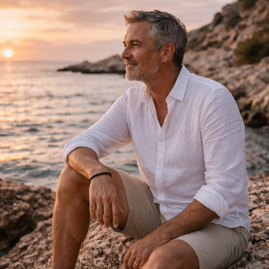 Man sitting on rocks by the ocean at sunset
