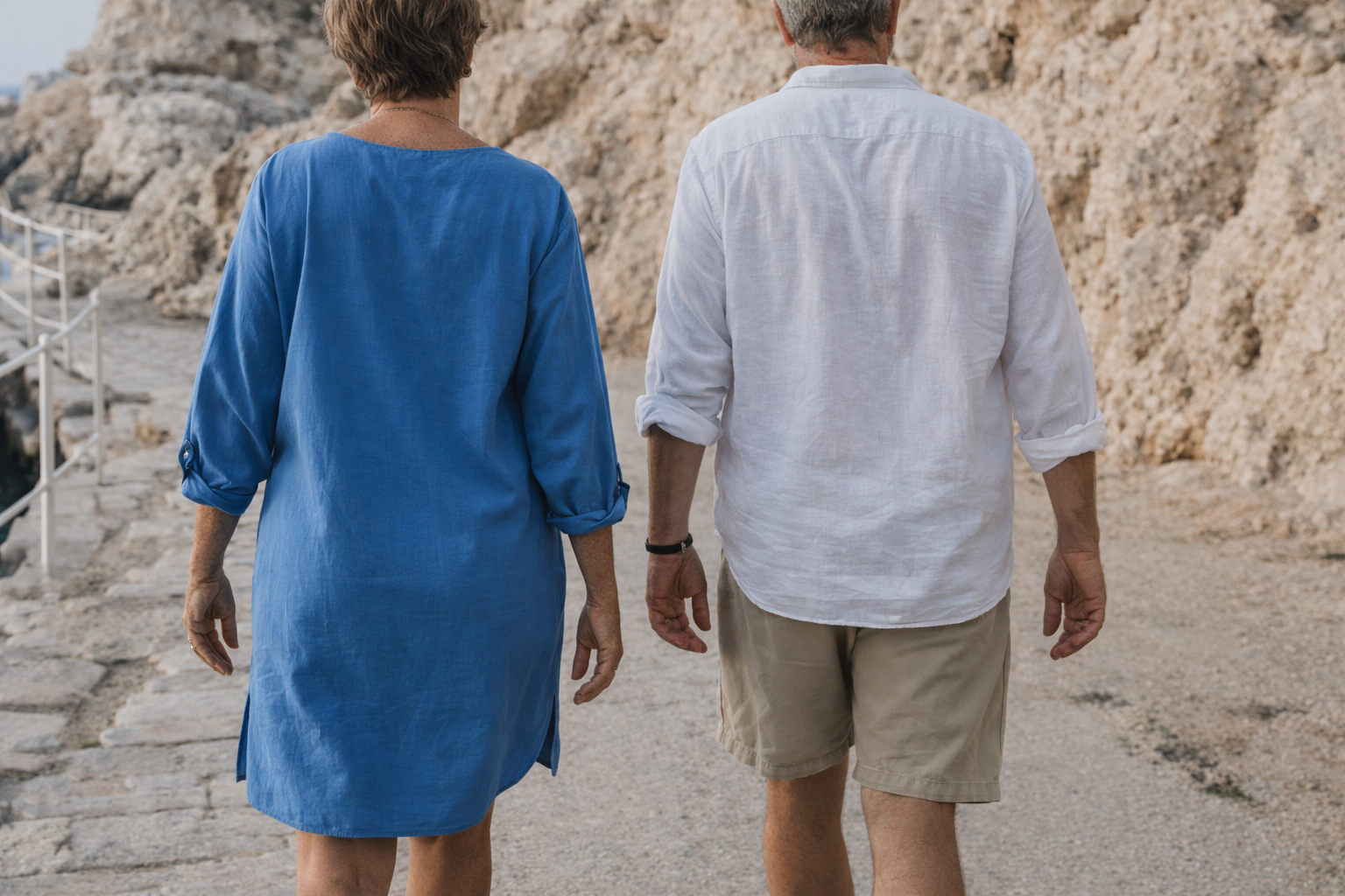 Two people walking along a coastal path with rocky cliffs in the background.